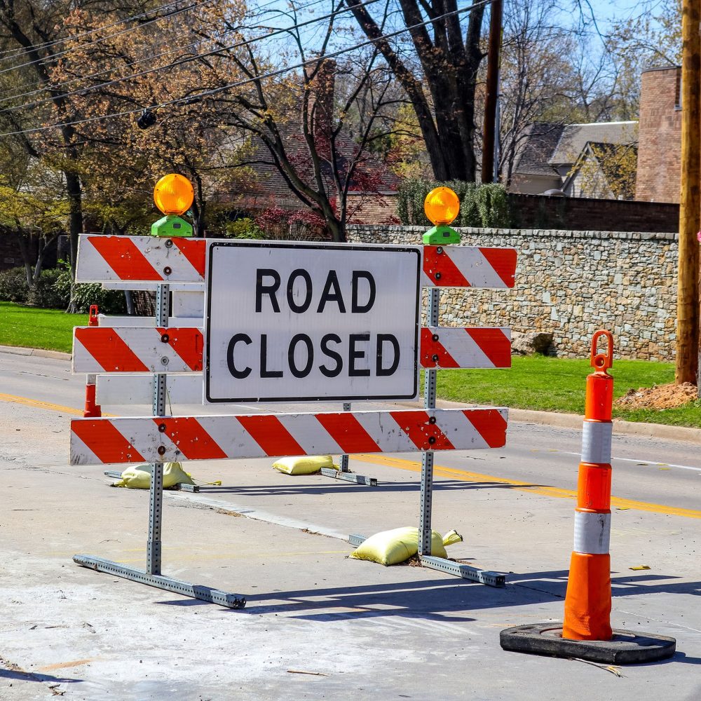 Road closed sign in the middle of four lane highway in residential neighborhood in early spring